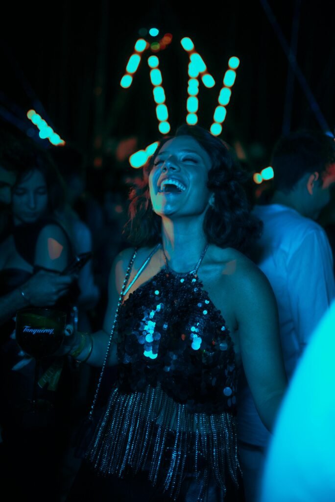 Woman in sequined dress laughing and dancing in a vibrant nightclub setting.